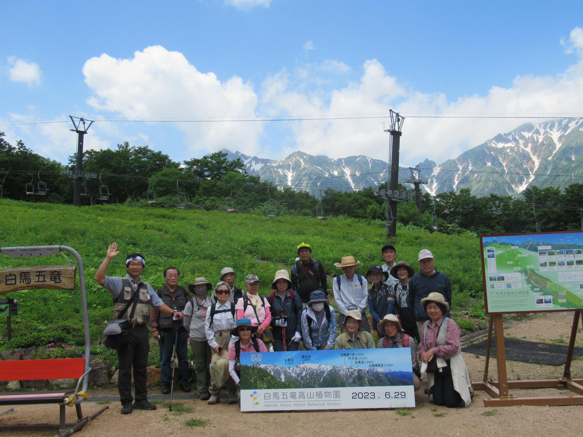白馬五竜高山植物園で五竜岳を背景に受講生16名とガイドが集合している写真