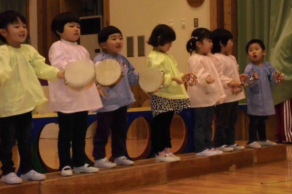 園児たちがタンバリンや鈴を持ち楽器を使って歌っている写真