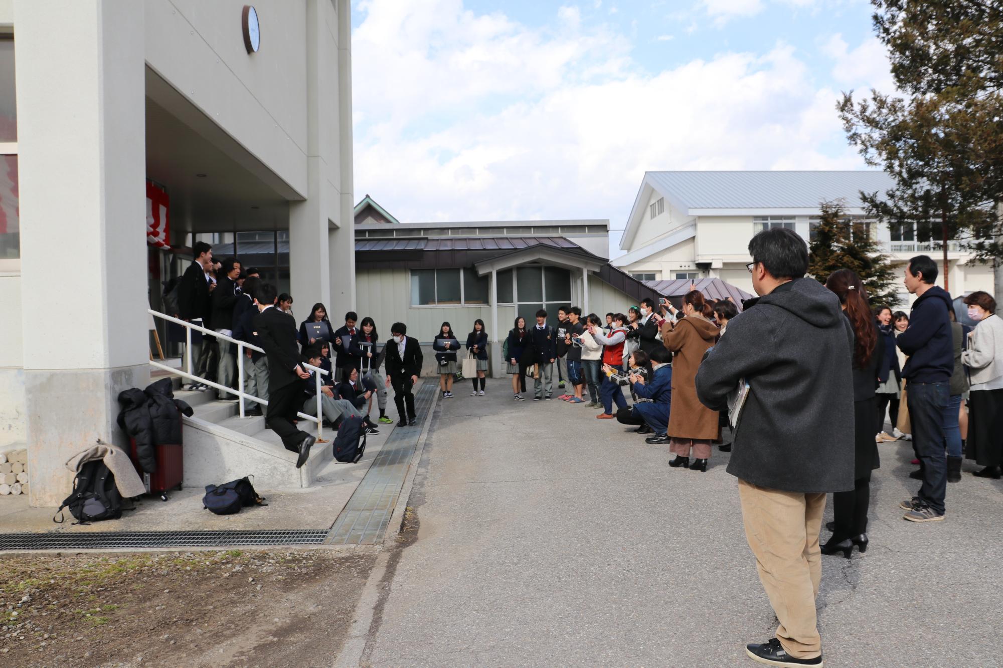 昇降口前の全景、卒業生とお出迎えの保護者や在校生