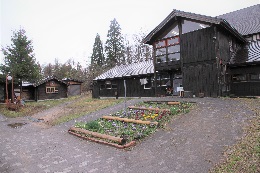 黒い木造の建物の前には花壇に色とりどりの花が咲く信州グリーンシェアスポットの白馬ノルウェービレッジ外観写真